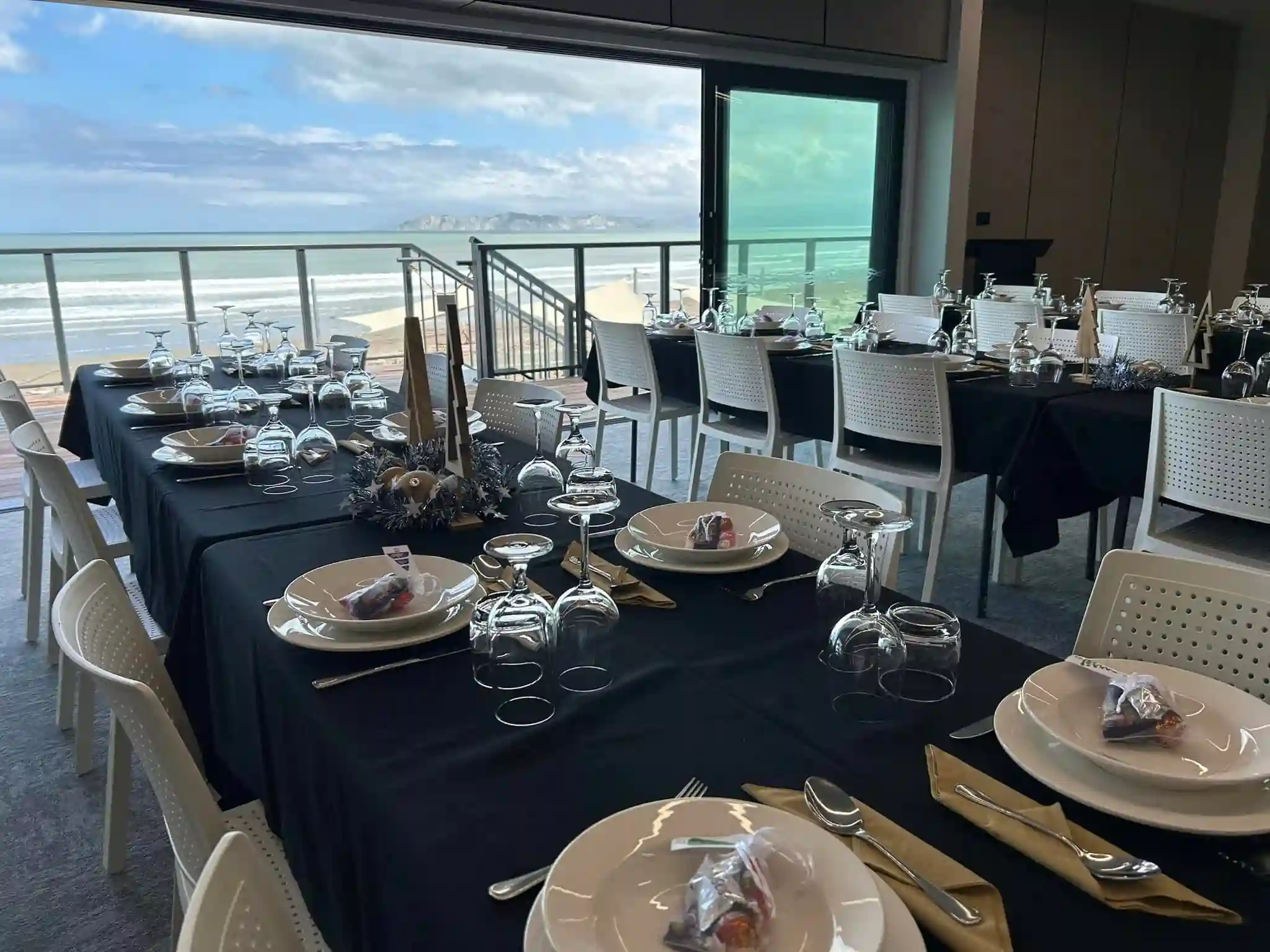 Christmas party dinner setup with black tablecloths and ocean views at a Gisborne function venue